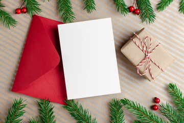 Christmas greeting card mockup with red envelope, gift box and decorated fir tree branches