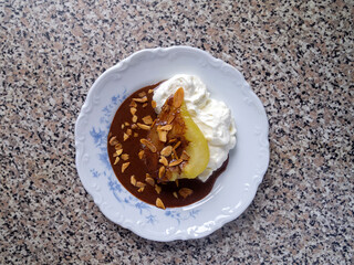 Top view of one poached caramelized pear with whipped cream, chocolate sauce and almond flakes. French dessert poire belle Helene.