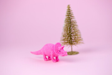 festive minimal greeting card with cute dinosaur and christmas tree on a pink background