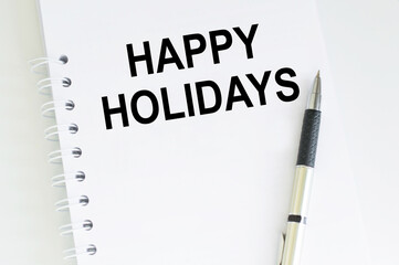 Happy Holidays Text on a white notepad on a table next to a pen.