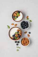 Homemade granola with berries and yoghurt. Bowl of Greek yogurt with almond nuts, oat granola and fresh blueberries on white background