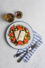 Traditional Greek rustic salad with tomatoes, cucumbers, onions, feta cheese, olive oil and herbs in plate on light background, top view