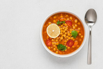 Chickpea lentil soup with vegetables, cilantro and lemon in light bowl on white table. Vegetarian soup top view