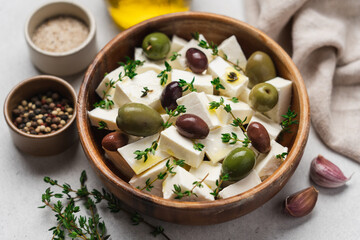 Soft feta cheese with olive oil, herbs and olives in wooden bowl on white background. Pieces of marinated cheese with fresh thyme