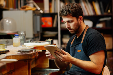 Young man works in his workshop consulting online orders on his digital tablet.