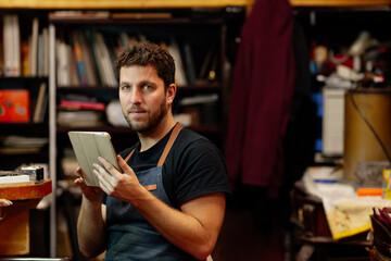 Young man works in his workshop consulting online orders on his digital tablet.