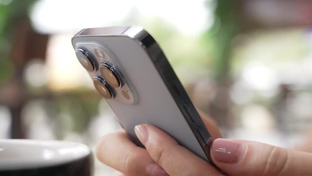 Frame with movement. Close-up of new fashionable modern Apple iphone 13pro in hands of human. Person is holding a phone and typing on the screen with his fingers. Beautiful bokeh, on a sunny day.