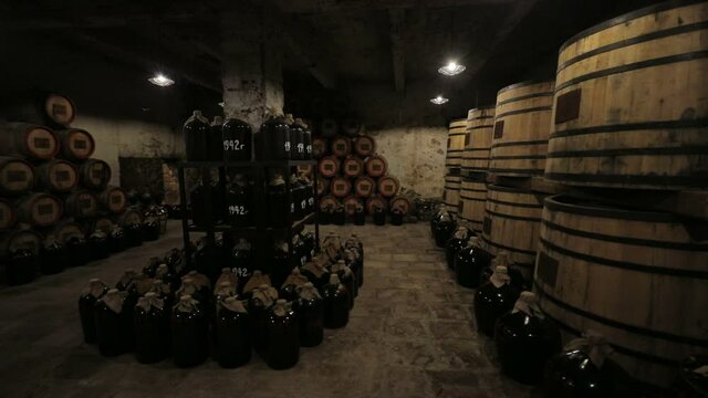 A Wine Cellar. Storage Room for Wine in Bottles and Barrels. Old wine in a dark underground vault. Wooden oak whiskey, wine, cognac, brandy or beer barrels. Bottles on wooden shelves.
