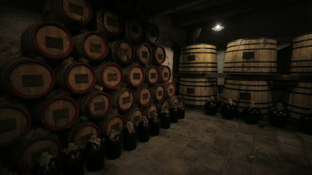 A Wine Cellar. Storage Room for Wine in Bottles and Barrels. Old wine in a dark underground vault. Wooden oak whiskey, wine, cognac, brandy or beer barrels. Bottles on wooden shelves.