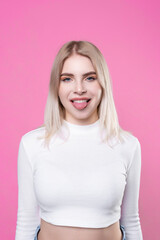Beautiful attractive young blonde. Studio portrait, close-up. Shows the language. Woman in white clothes, on pink isolated background