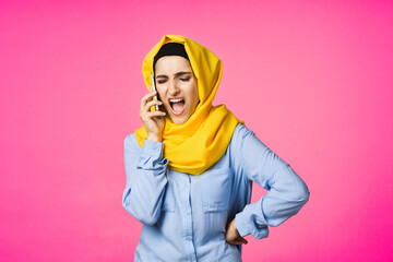 muslim woman in yellow hijab talking on the phone technology pink background