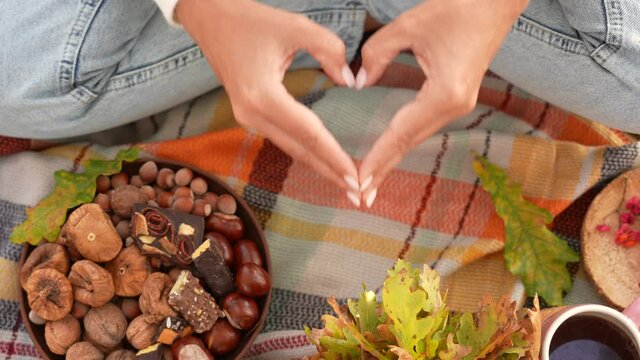 Close-up top view 4k video footage of two female hands making beautiful heart shape gesture with her fingers isolated on bright autumn decor and picnic blanket background