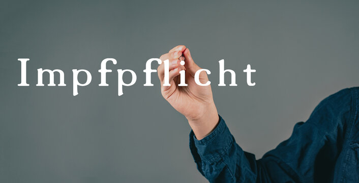 Mandatory vaccination is standing in german language on a grey background, hand with a pen is writing the message