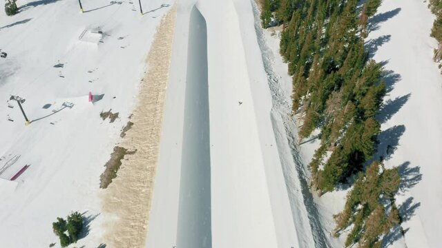 4K aerial skiing and snowboarding aerial through the soft light snow flakes. Skilled professional snowboarder riding and jumping above half pipe on white snowy ski slope on winter vacation day, USA