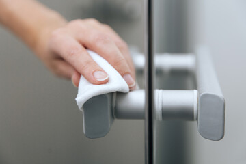 Cleaning glass door handles with an antiseptic wet wipe. Sanitize surfaces prevention in hospital and public spaces against corona virus. Woman hand using towel for cleaning home room door link.