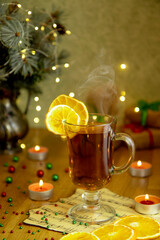 selective focus on a mug of hot black tea, smoke over the mug and dried oranges against the background of a Christmas tree and blurry specks of garlands sweet mood delicious healthy desserts