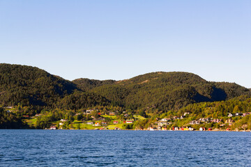 Fototapeta na wymiar Colorful traditional Norwegian houses near the sea with green forest on mountains and blue sky