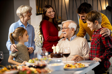 Family celebrating grandfather birthday with cake and candles at home