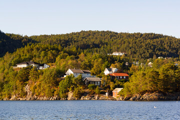 Colorful traditional Norwegian houses near the sea with green forest on mountains and blue sky