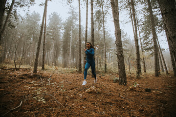 Naklejka na ściany i meble Young woman running toward camera on the forest trail at autumn