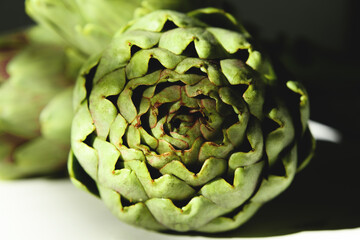 Fototapeta premium Fresh artichoke on a white wooden background with beautiful daylight shadow, close up. One raw organic artichoke flower