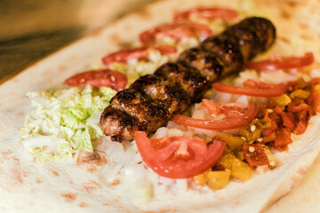 Shawarma with meat kebabs, with sauce, tomatoes, peppers, cheese, herbs, cabbage, onions and garlic on ruddy pita bread, lying on a wooden board