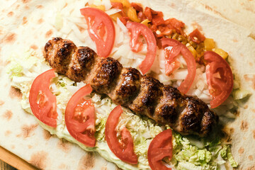 Shawarma with meat kebabs, with sauce, tomatoes, peppers, cheese, herbs, cabbage, onions and garlic on ruddy pita bread, lying on a wooden board