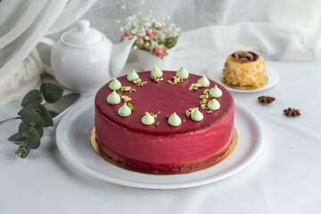 modern mousse cake covered with pink glaze decorated with merinques and teapot on the table