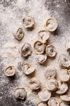 Lots of homemade dumplings on table with flour. Raw ravioli are ready for cooking. Close-up, selective focus.