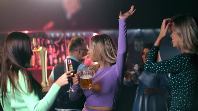 Overjoyed female friends dancing drinking beer champagne and cocktail at night club bar discotheque