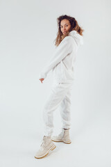 Smiling woman with thick curly hair in a white suit of hoodies and sweatpants.