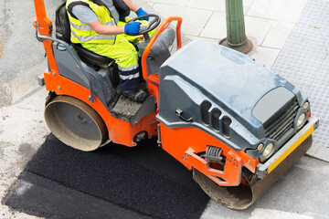construction worker with small steamroller for repairing potholes and paving the road in city street