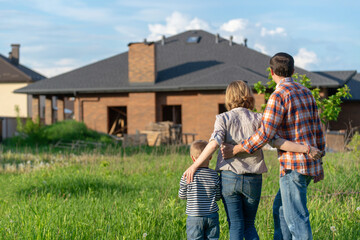 Back view of happy family is standing near their new modern house and hugging