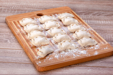 Fototapeta na wymiar Handmade pierogies on a wooden board. Freshly made dumplings