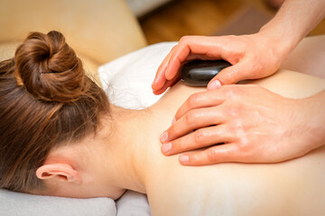 Obraz na płótnie Canvas Hot stone massage therapy. Caucasian young woman getting a hot stone massage on back at spa salon