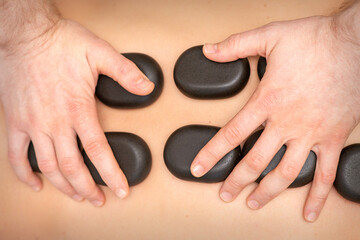 Obraz na płótnie Canvas Hot stone massage therapy. Caucasian young man getting a hot stone massage on back at spa salon