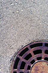 Part of a round manhole with grating on the asphalt.