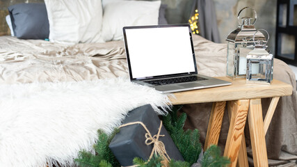 Opened laptop with blank screen on bed in cozy bedroom decorated for Christmas holidays with Christmas tree
