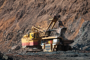Fototapeta premium Quarry excavator loading iron ore into the heavy dump truck in iron ore open cast mine