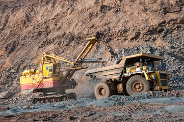 Quarry excavator loading iron ore into the heavy dump truck in iron ore open cast mine