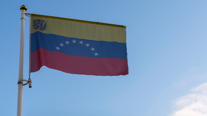 Fototapeta na wymiar National flag of Venezuela on a flagpole in front of blue sky with sun rays and lens flare. Diplomacy concept.