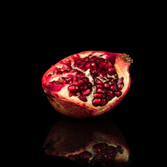 half ripe pomegranate fruit, on a black background in isolation, with reflection