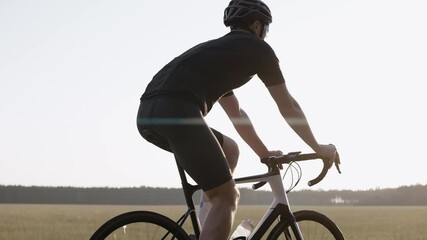 Close-up of man riding a road bike at the sunset on a highway, wearing helmet and sunglasses. Workout on triathlon bike. Side shot of cyclist in black outfit riding road bicycle. 50 fps. 4k footage