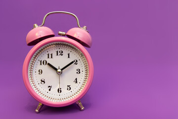 Pink old clock on a purple background, sounds loud. Place for text, signature, product name. It's time to celebrate and make presents. An isolated alarm clock wakes you up to go to school, university.