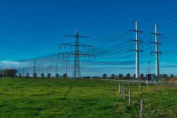 Fototapeta na wymiar Traditional and modern electricity pylons a green field in the agricultural province of Groningen, the Netherlands 