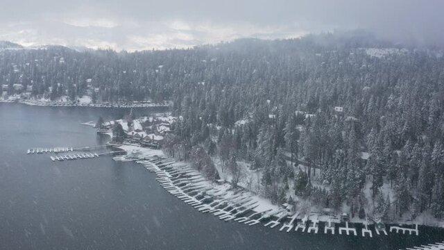 Winter snowfall, mountain forest aerial. Breathtaking natural landscape, frozen forest, snow falling at mountain lake. Wonderland village with boat landing docks at waterfront forest cabins, Arrowhead
