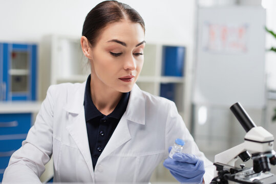 brunette scientist in white coat holding coronavirus vaccine in laboratory.