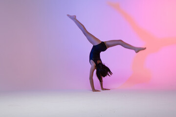 child athlete gymnast performing gymnastic exercises on the ground, training for competition, colorful background in a studio.
