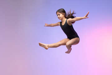 young gymnast athlete performing jumps, training for competition, colorful background in a studio.