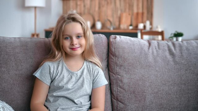 Portrait happy cute little blonde girl sitting couch at living room interior with positive emotion